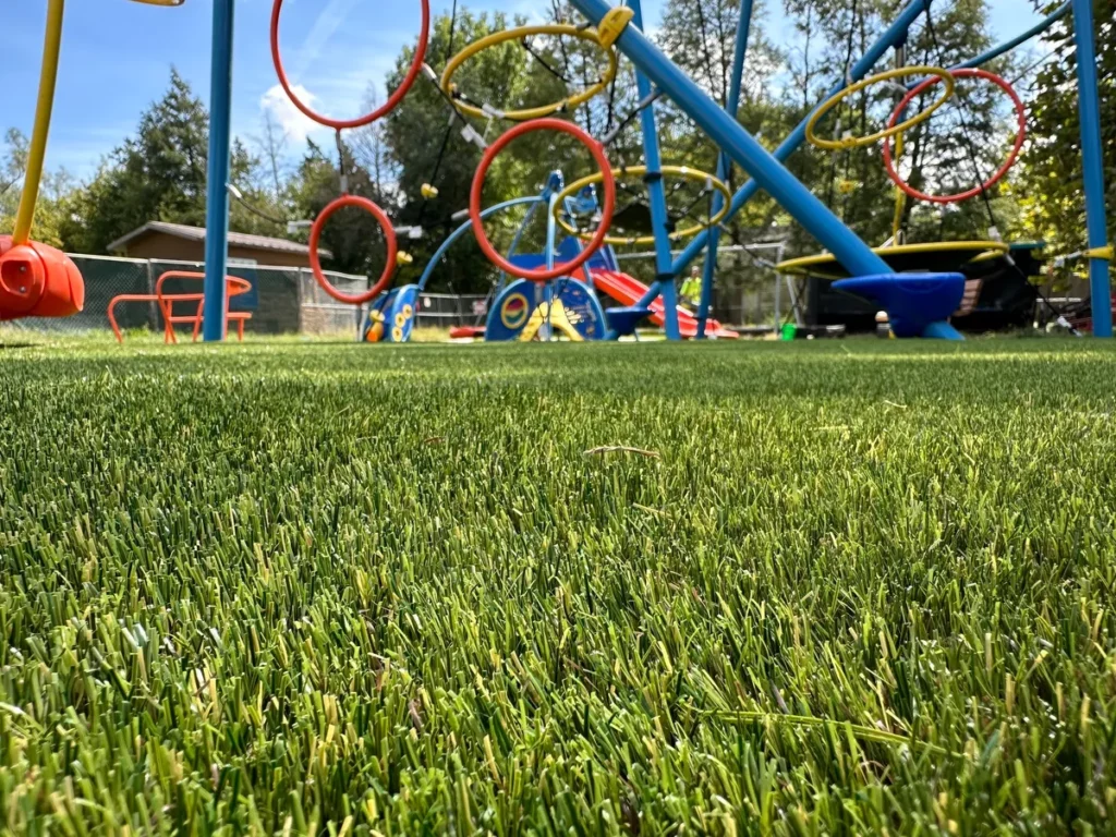 Artificial turf playground surface at Indianapolis municipal park with colorful play structures, hoops, and slides in background.