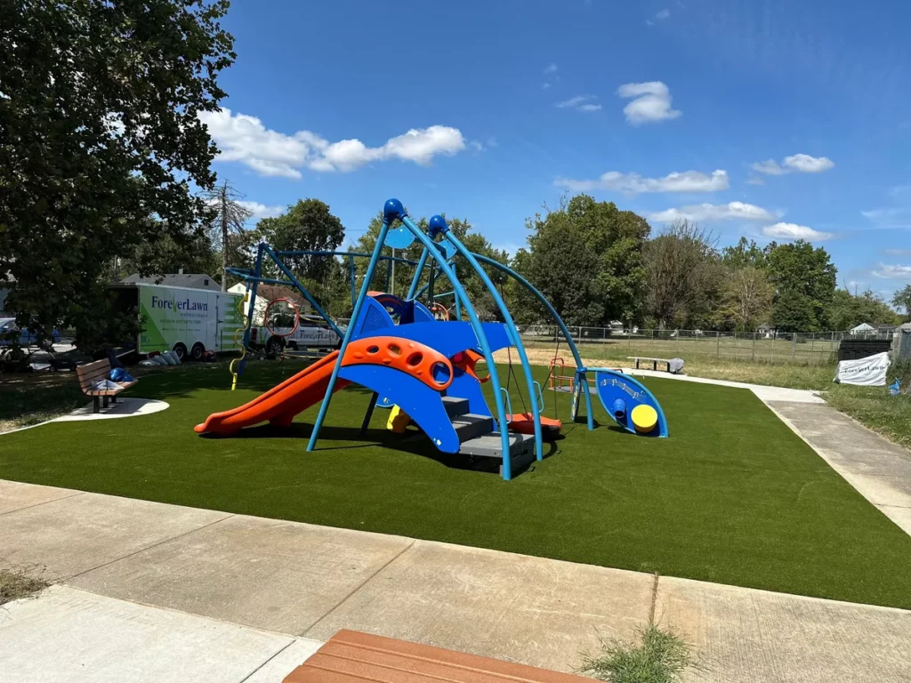 Blue and orange playground set on freshly installed artificial turf at Indianapolis municipal park by ForeverLawn.