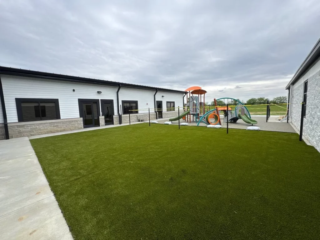 Artificial playground turf installed at school courtyard with colorful play structure, slides, and modern white building exterior.
