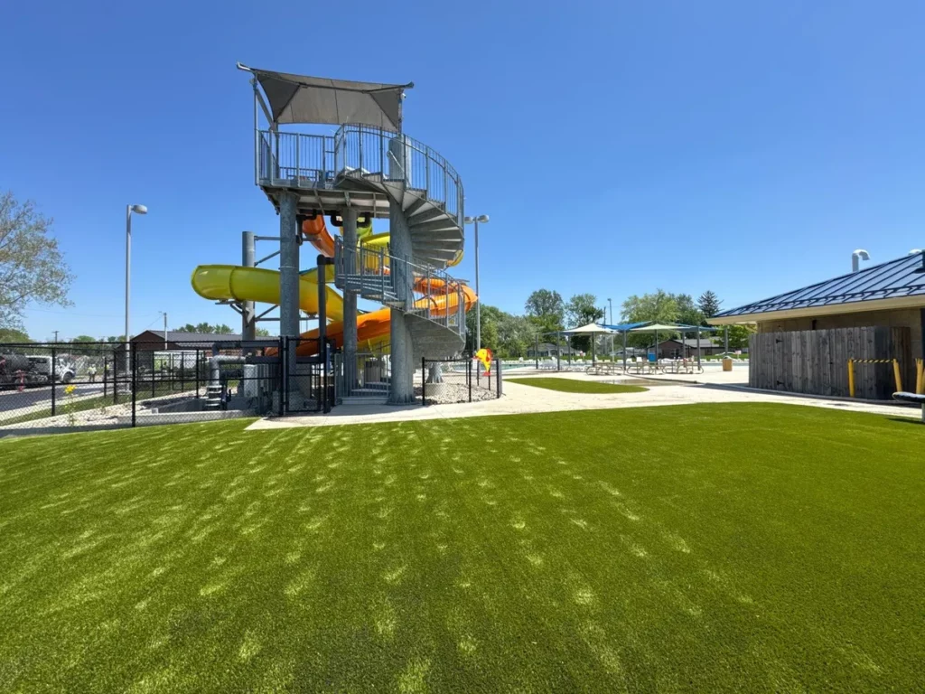 Bright green Playground Grass Ultra artificial turf surrounds a municipal water park with colorful orange and yellow spiral water slides.