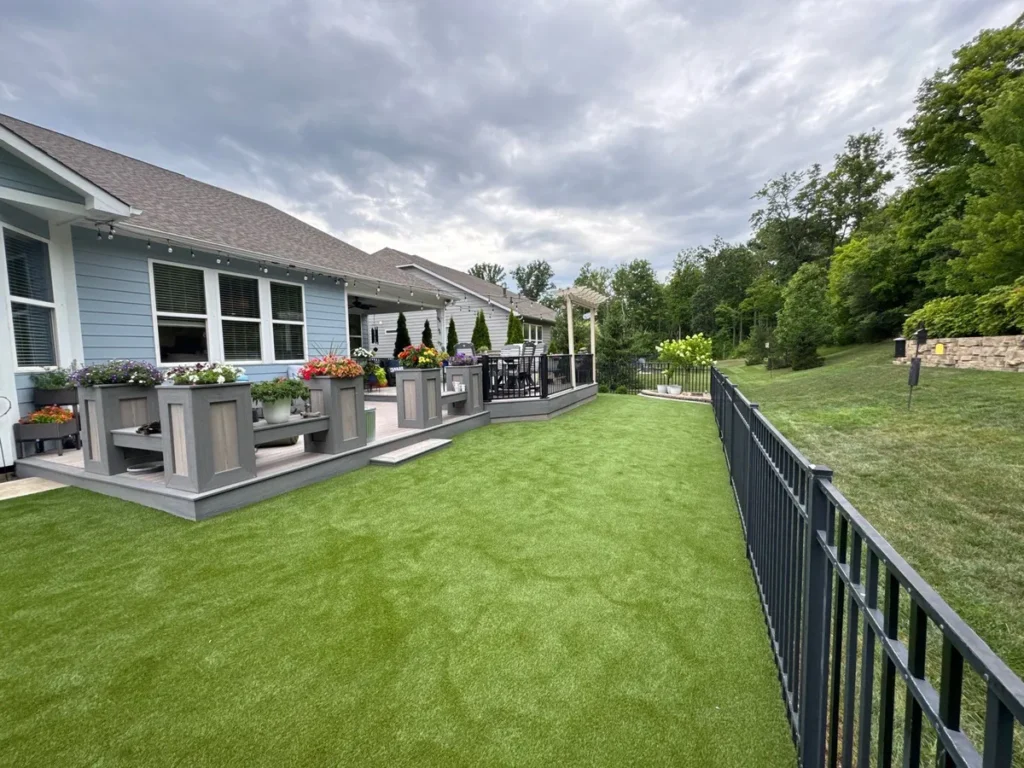 K9Grass Endura artificial turf installed in fenced suburban backyard beside gray composite deck with flower planters.