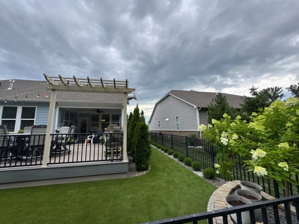 K9Grass Endura artificial turf pet yard with pergola deck, black aluminum fence, arborvitae, and hydrangeas in suburban backyard.