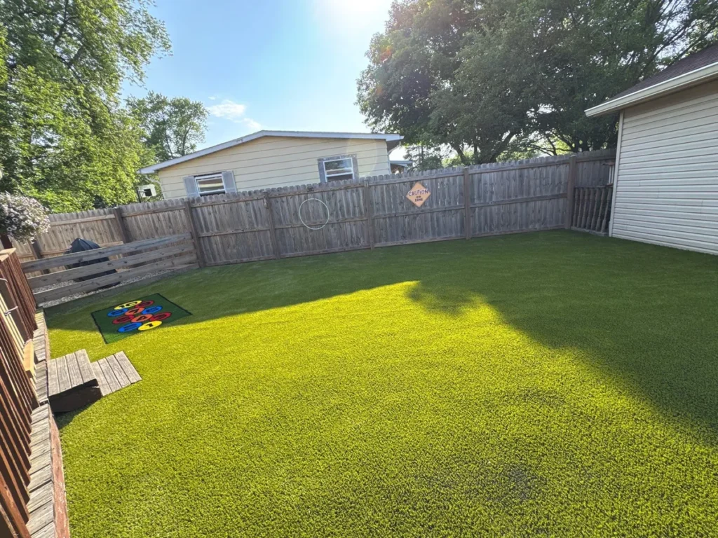 Lush artificial playground turf installed in fenced residential backyard with ring toss game mat and hula hoop target.
