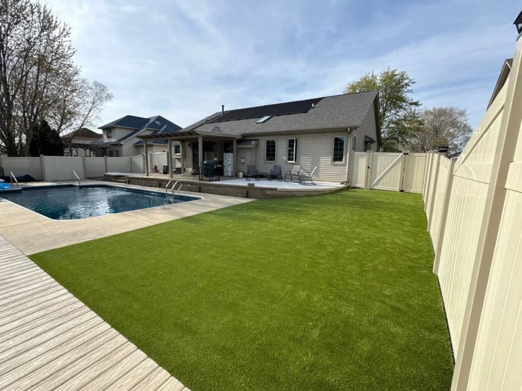 K9Grass artificial turf installed in fenced suburban backyard beside inground pool and raised patio deck
