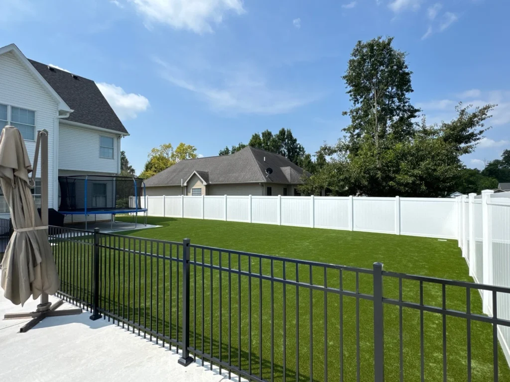 K9Grass Endura artificial turf installed in large fenced suburban backyard with white vinyl privacy fence and black iron railing.