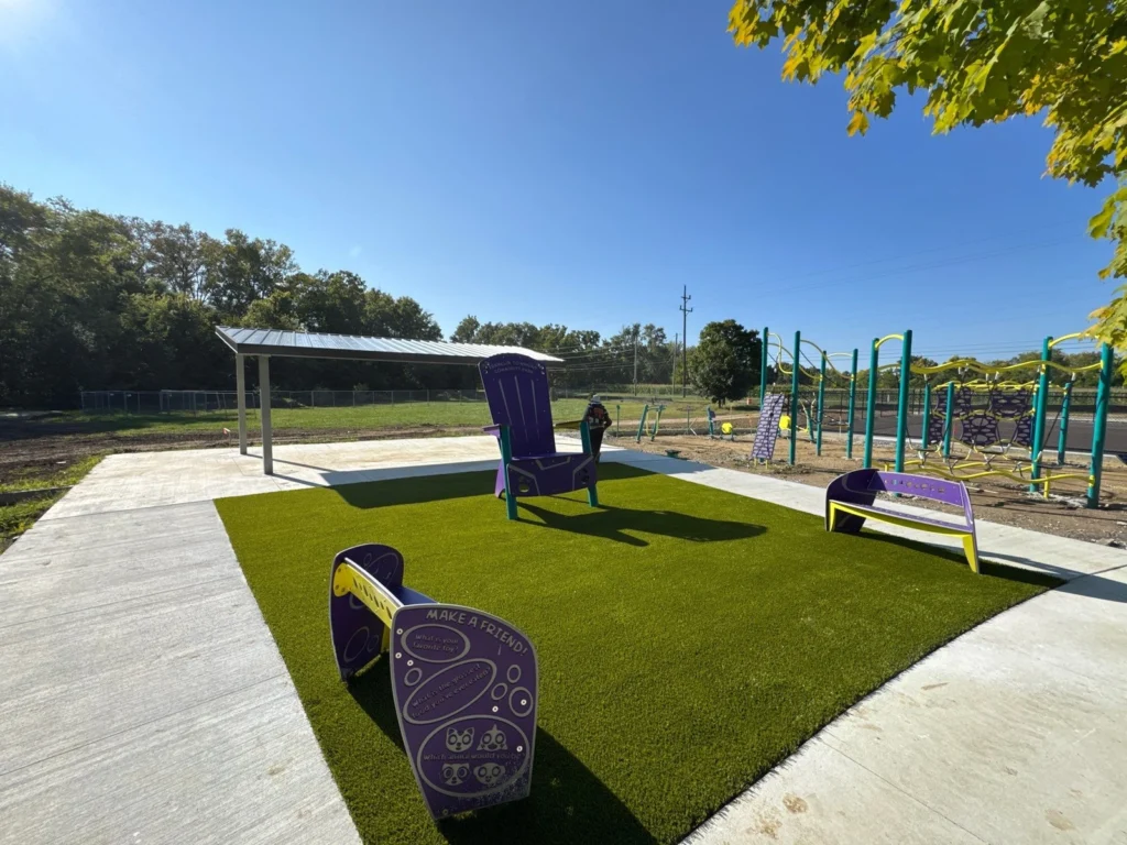 Playground Grass Ultra artificial turf installed at Franklin Township Park with purple benches, oversized chair, pavilion, and fitness equipment.