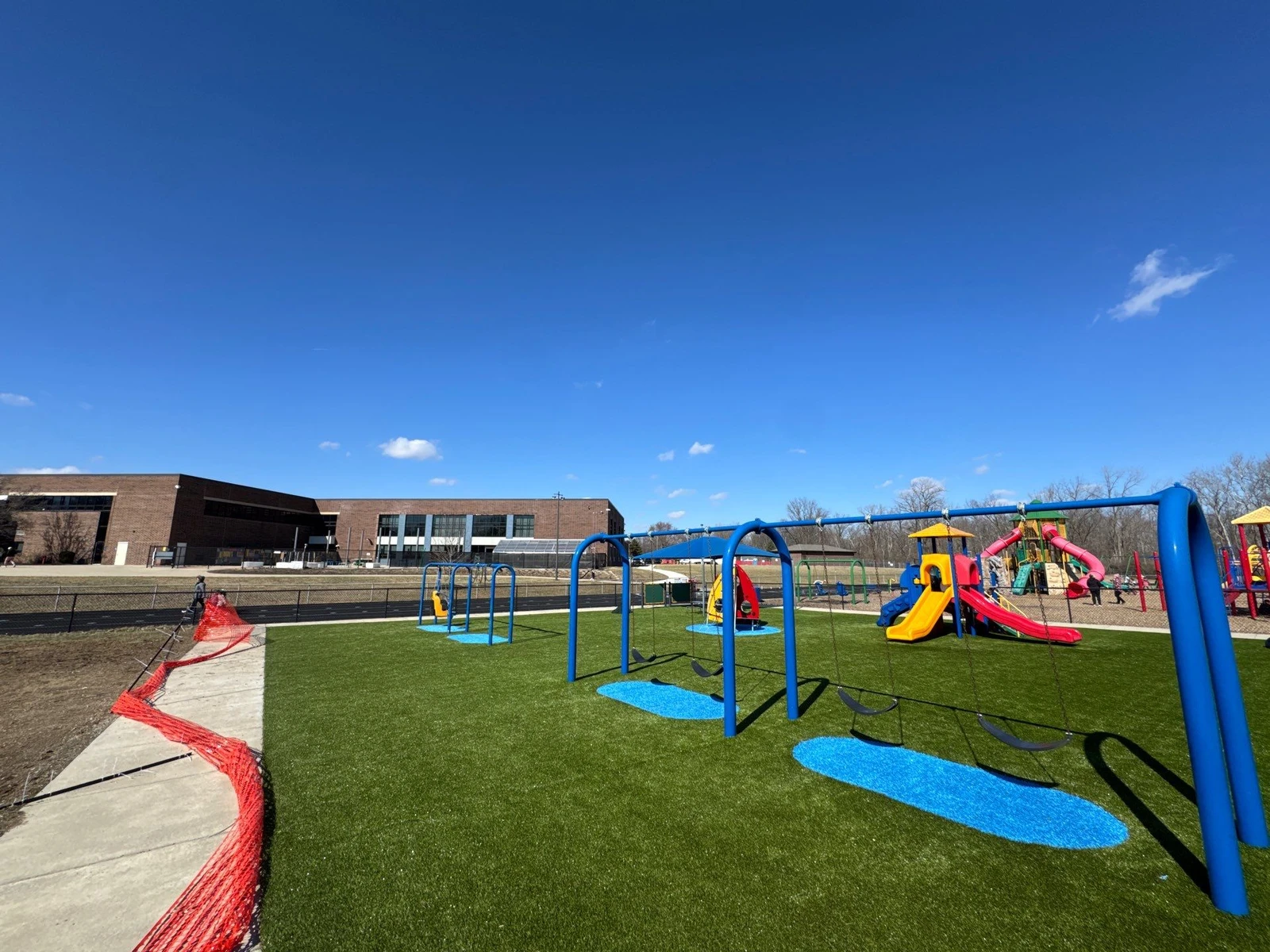 ForeverLawn Playground Grass installed at Clarks Creek Municipal Park in Plainfield with blue swing sets, colorful play structures, and blue safety zones.