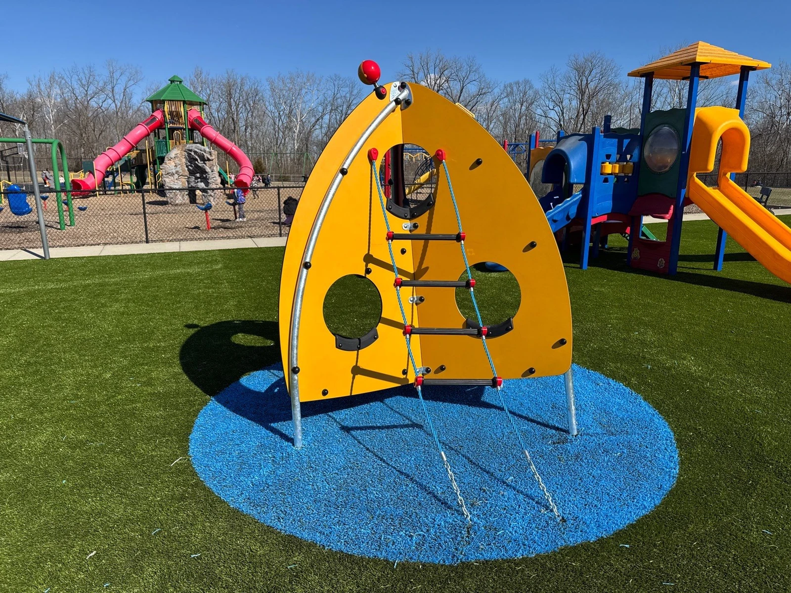 Yellow arch climbing structure on blue ForeverLawn Playground Grass circle pad at Clarks Creek Park, Plainfield municipal playground