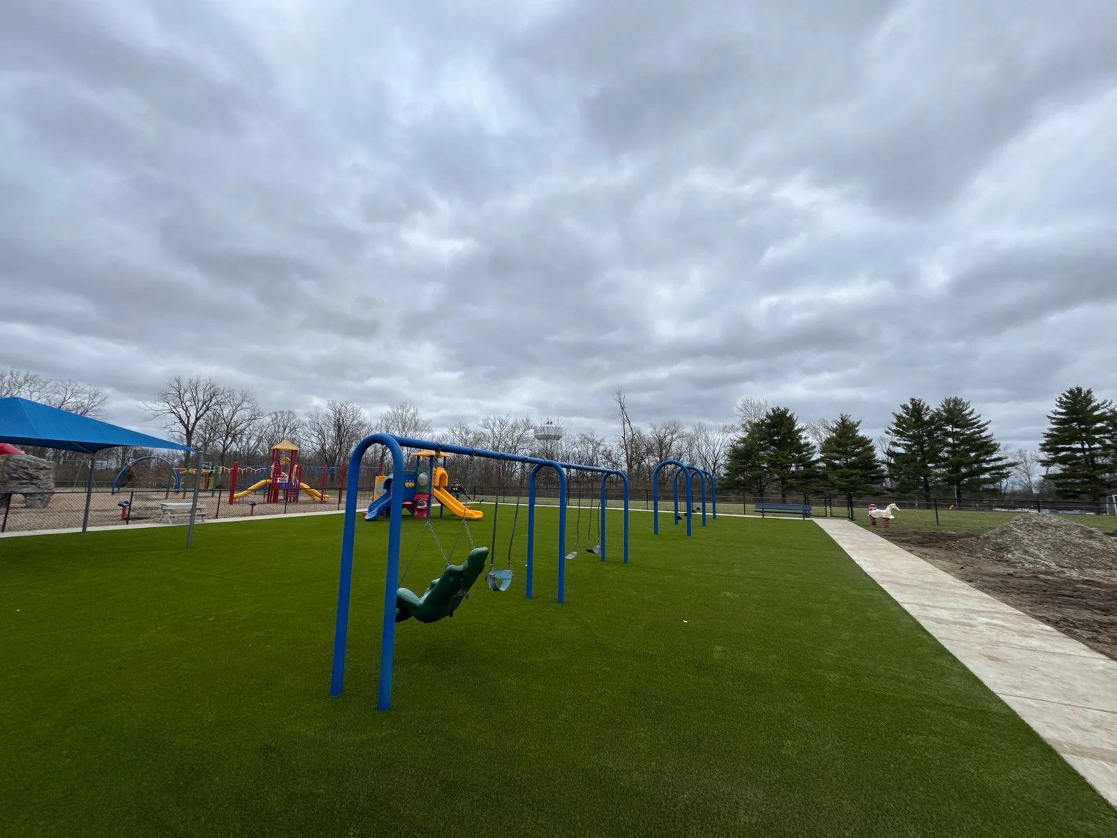 Blue swing set and colorful play structures on lush artificial Playground Grass at Clarks Creek Municipal Park in Plainfield, IN.