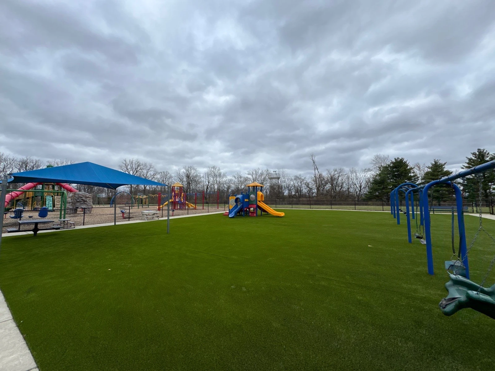 Vibrant artificial playground grass installation at Clarks Creek Municipal Park in Plainfield with colorful play structures and swing sets.