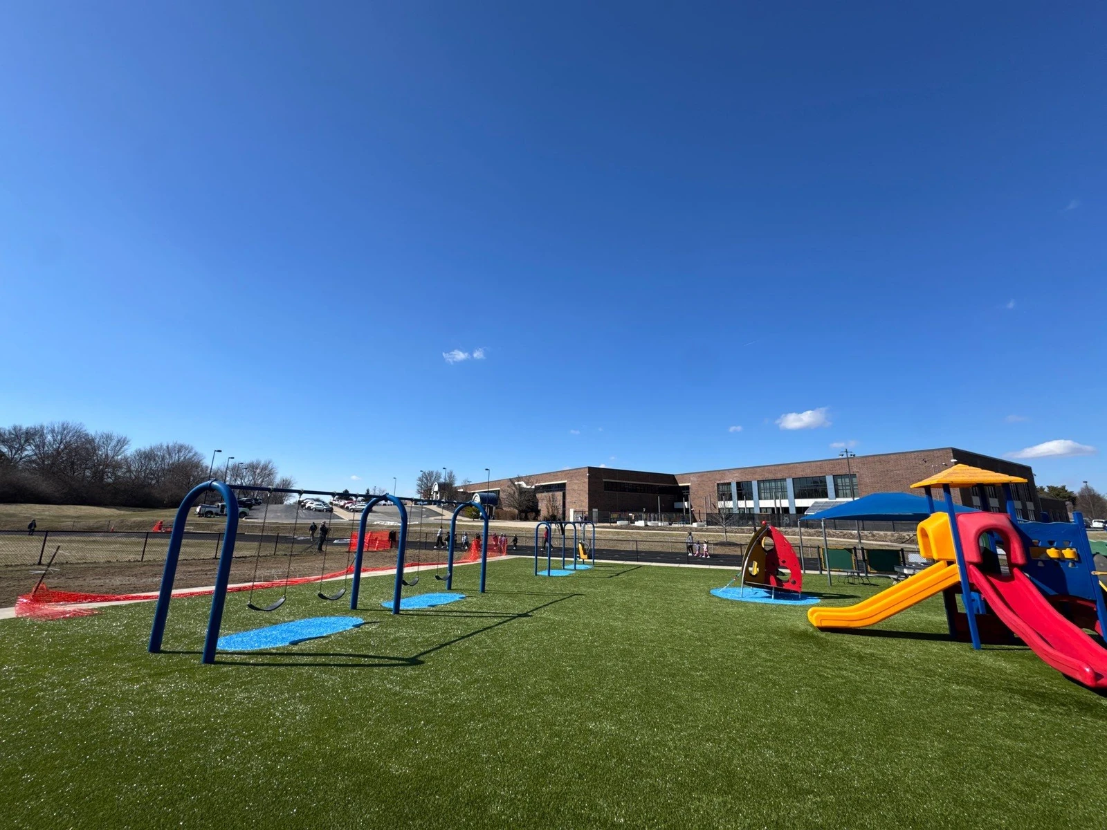 New Playground Grass artificial turf installed at Clarks Creek playground in Plainfield with colorful swing sets and slides under blue sky.