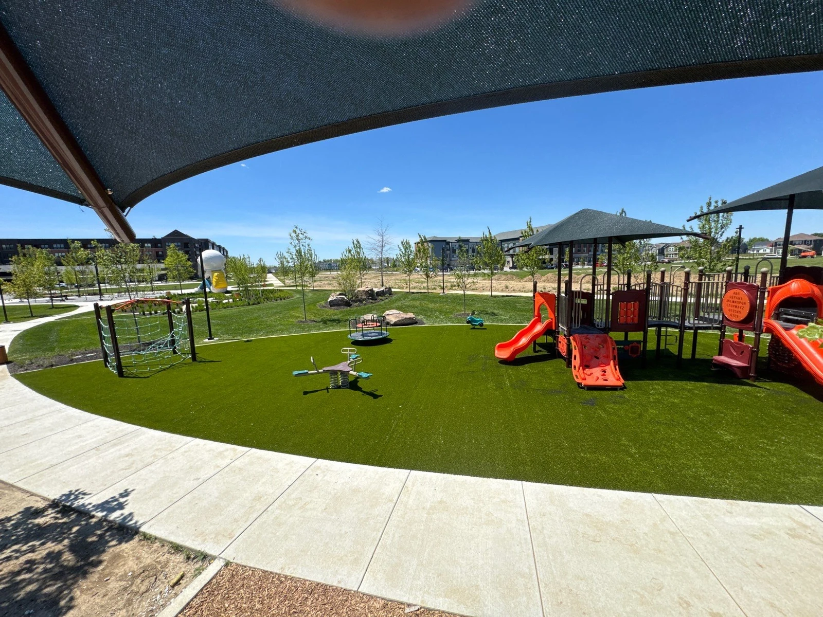 ForeverLawn Playground Grass covering large municipal park play area with orange slides, climbing structures, and shade sails in Plainfield, IN.