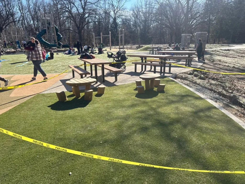 ForeverLawn Playground Grass Quest installed at Holliday Park, Indianapolis, with picnic tables, caution tape, and playground equipment visible.