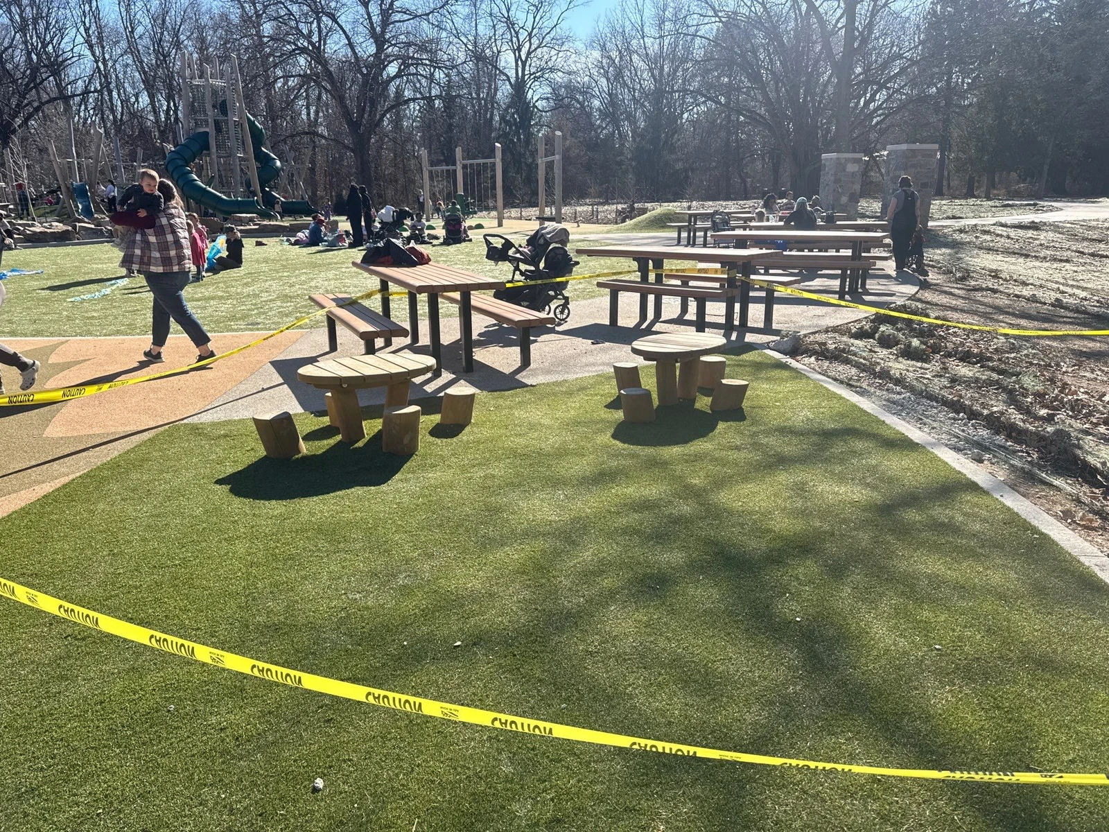 ForeverLawn Playground Grass Quest installed at Holliday Park, Indianapolis, with picnic tables, caution tape, and playground equipment visible.