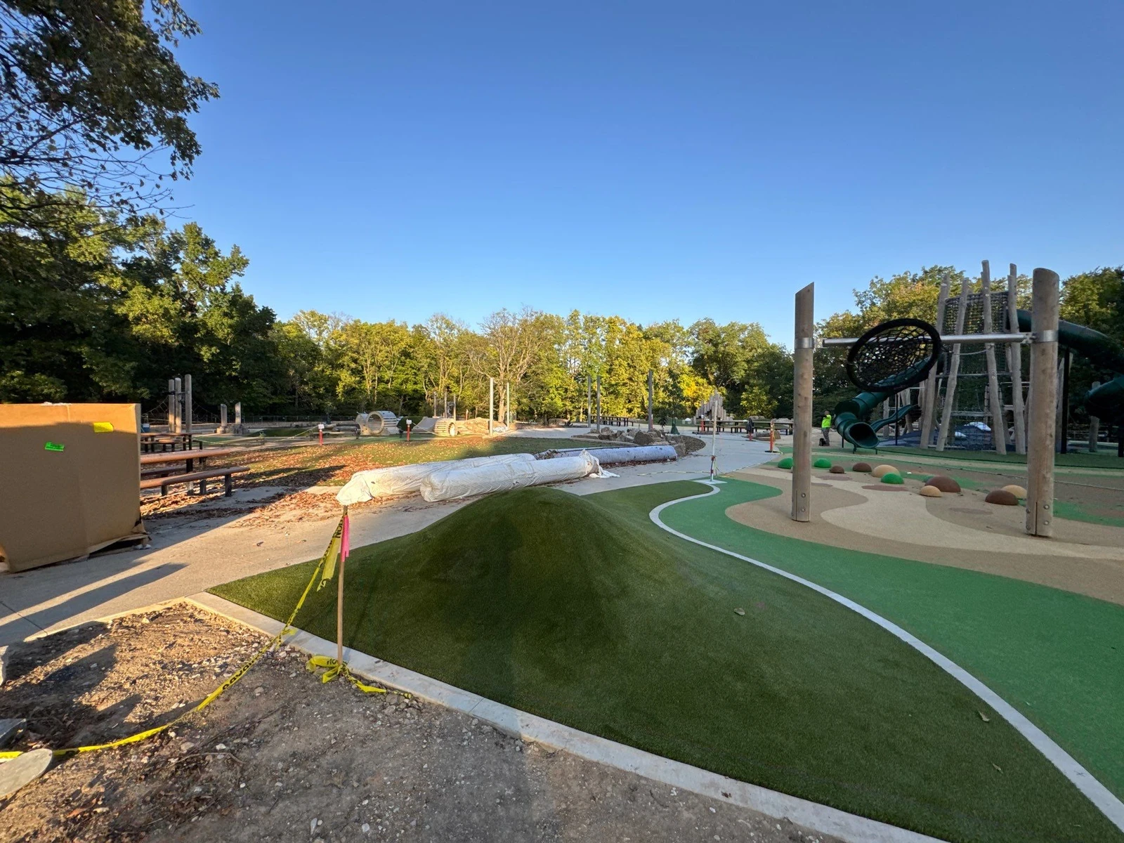 ForeverLawn Playground Grass Quest installation underway at Holliday Park, showing artificial turf mounds, climbing structures, and rubber safety surfacing.