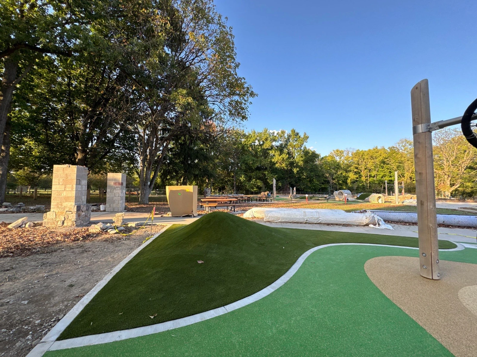 Artificial turf mound and curved green playground surface installed at Holliday Park, with stone pillars and play structures under construction.