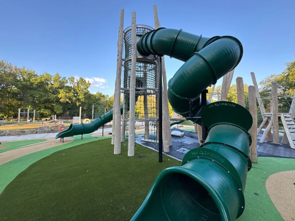 Green tube slide and rope climbing tower on Playground Grass Quest artificial turf at Holliday Park municipal playground.