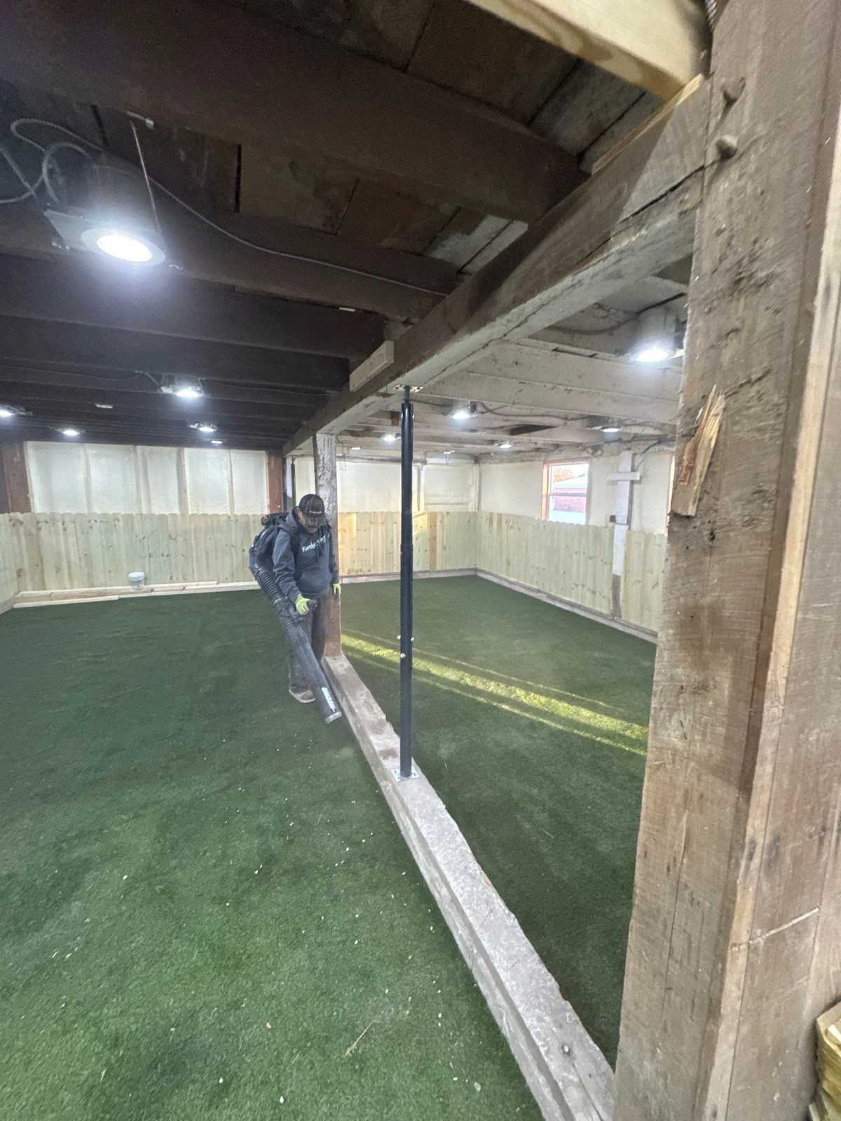 Worker using backpack blower on K9Grass Elite artificial turf inside rustic barn dog park facility in Pittsboro, IN.