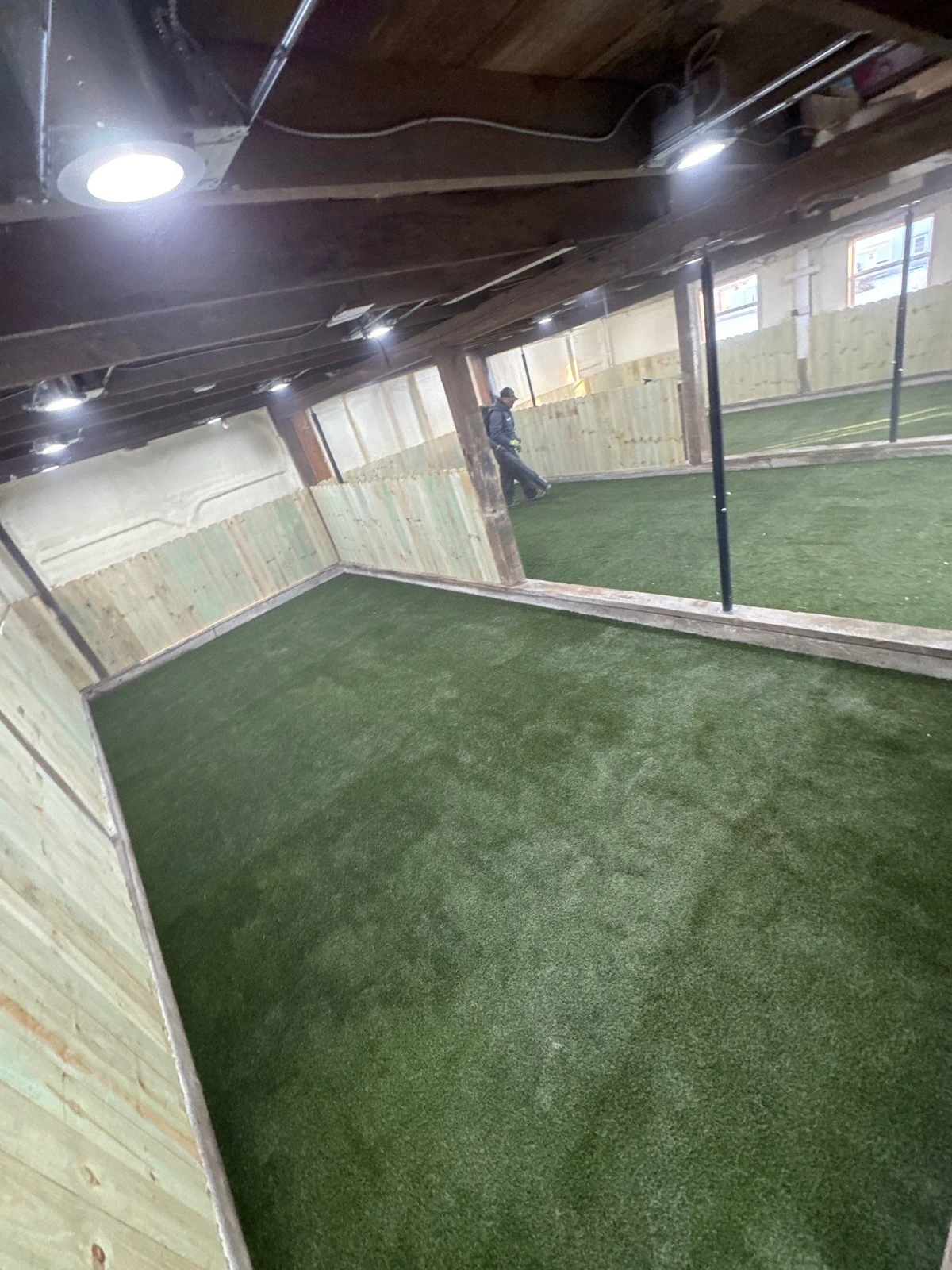 Indoor dog park with K9Grass Elite artificial turf, wood panel walls, overhead lighting, and metal posts in Pittsboro, IN.