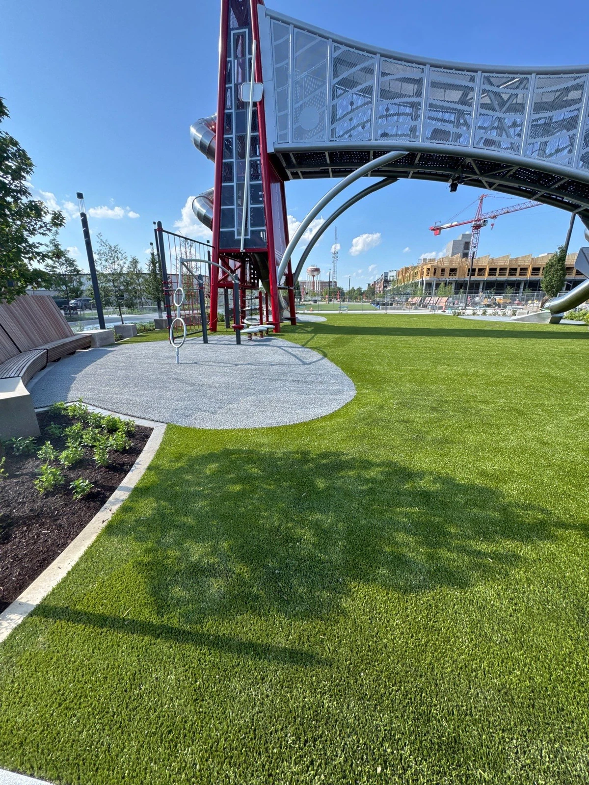 K9Grass artificial turf surrounds a large modern playground structure at The Monon, with rubber safety surfacing and curved seating nearby.