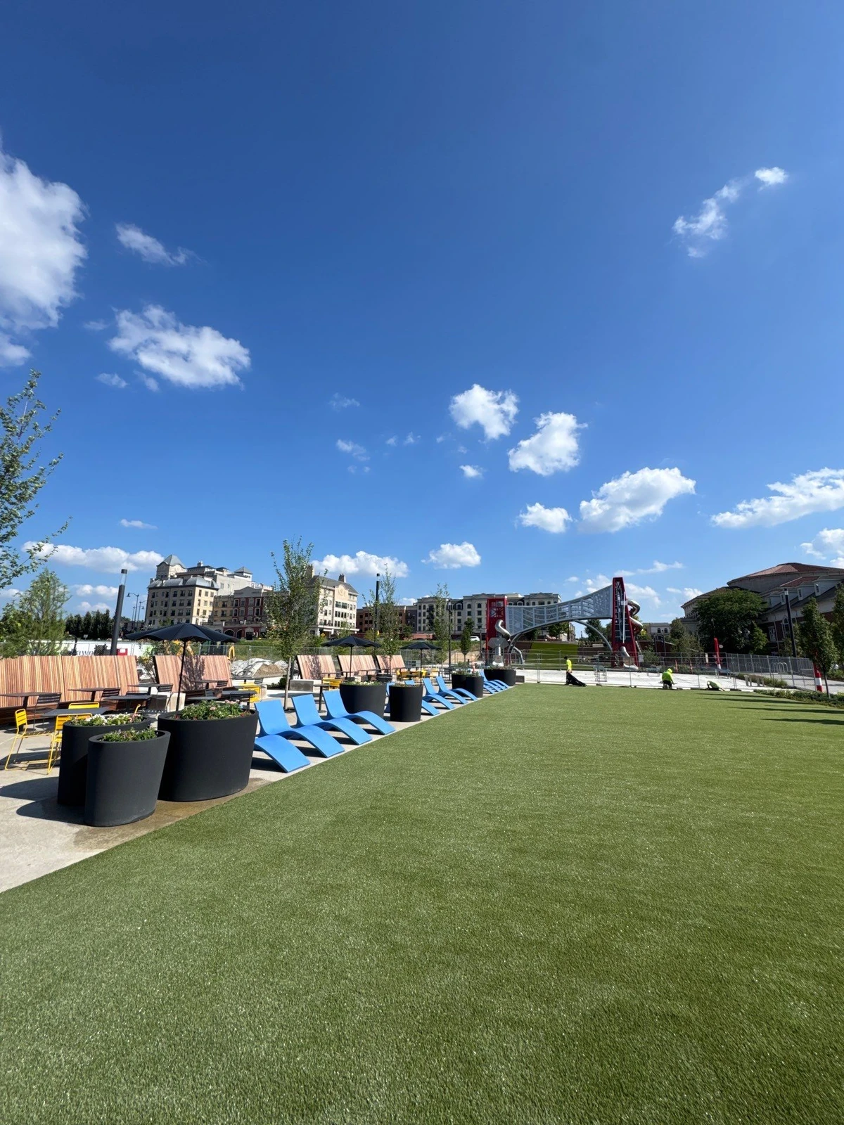 K9Grass pet turf lawn at The Monon with blue lounge chairs, planters, and urban skyline under sunny skies.