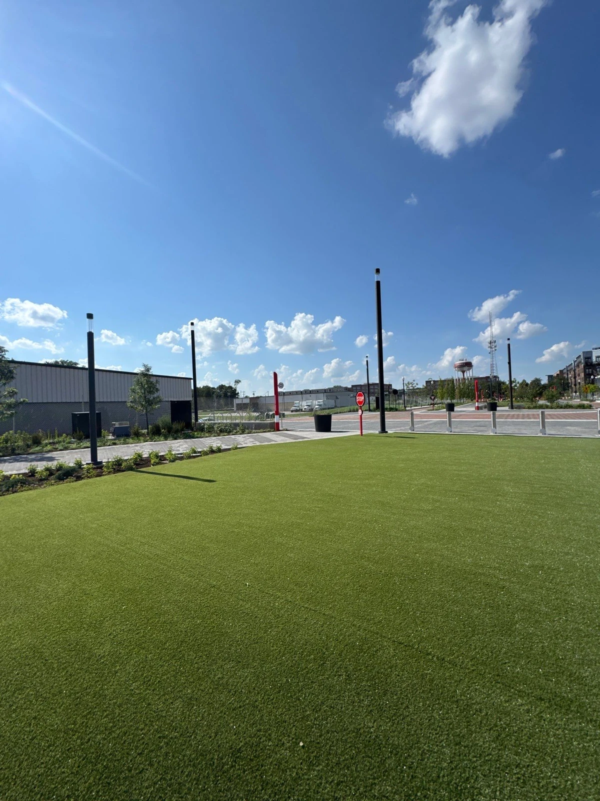 Large K9Grass pet turf area at The Monon, surrounded by light poles, stop signs, and urban development under blue sky.