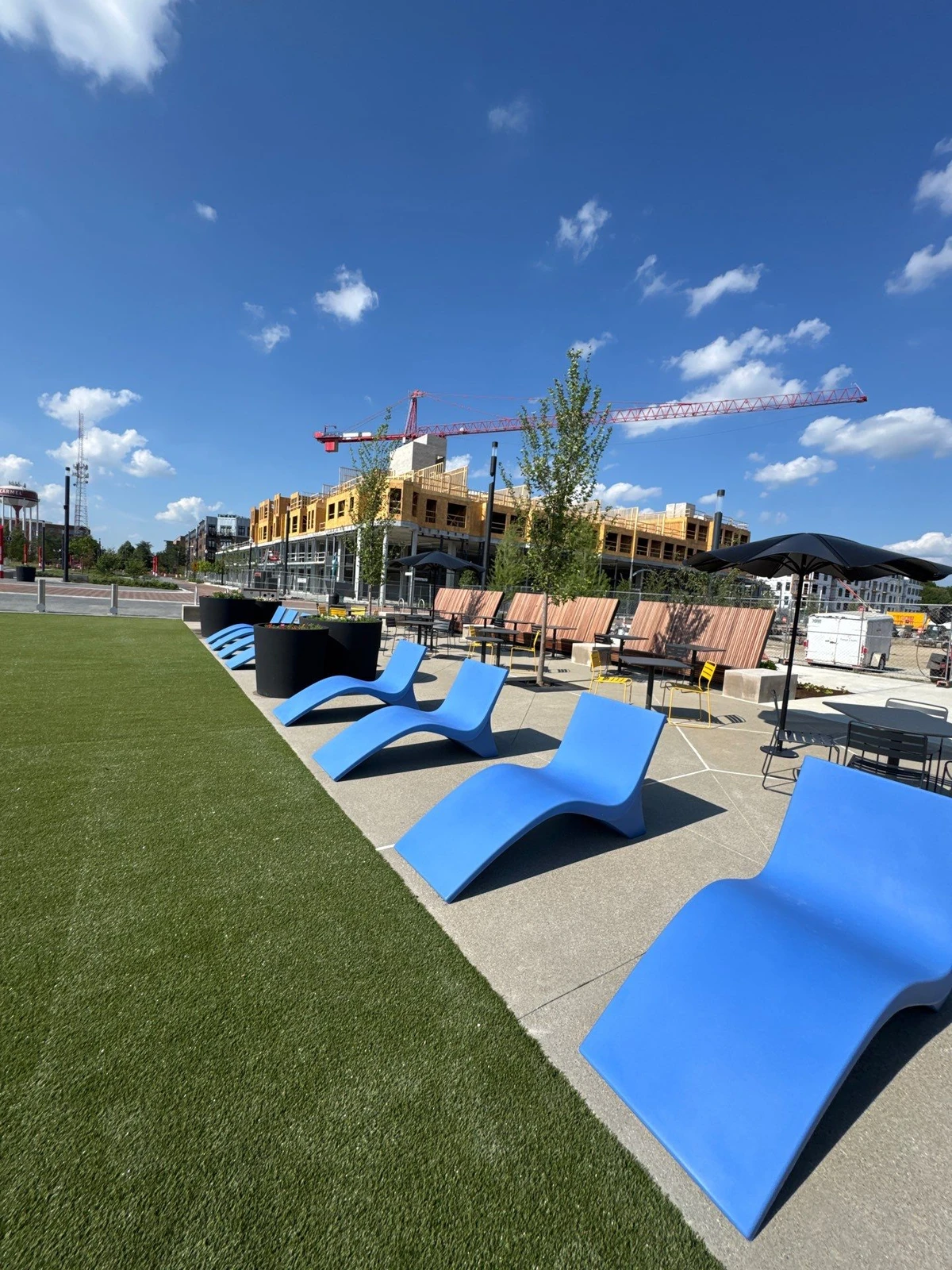 K9Grass pet turf installation beside concrete patio with blue lounge chairs at The Monon, construction crane in background.