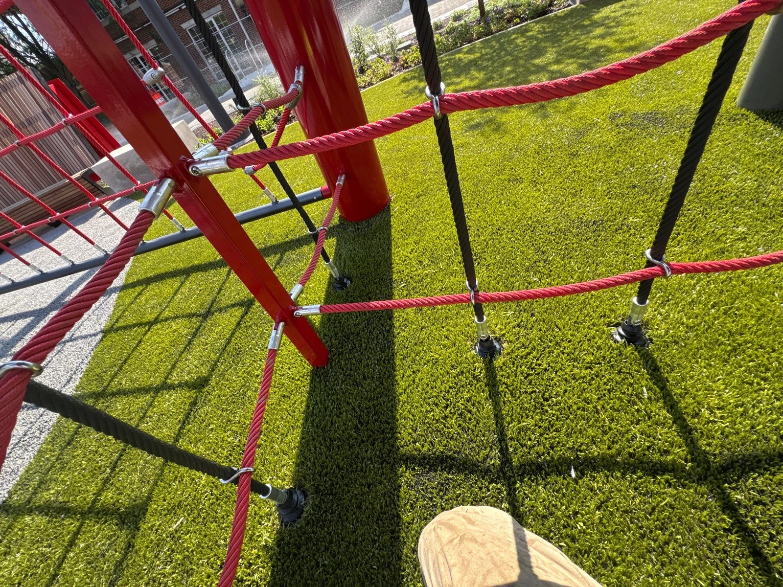 Red rope climbing structure installed over K9Grass artificial turf at The Monon, with brick building visible in background.