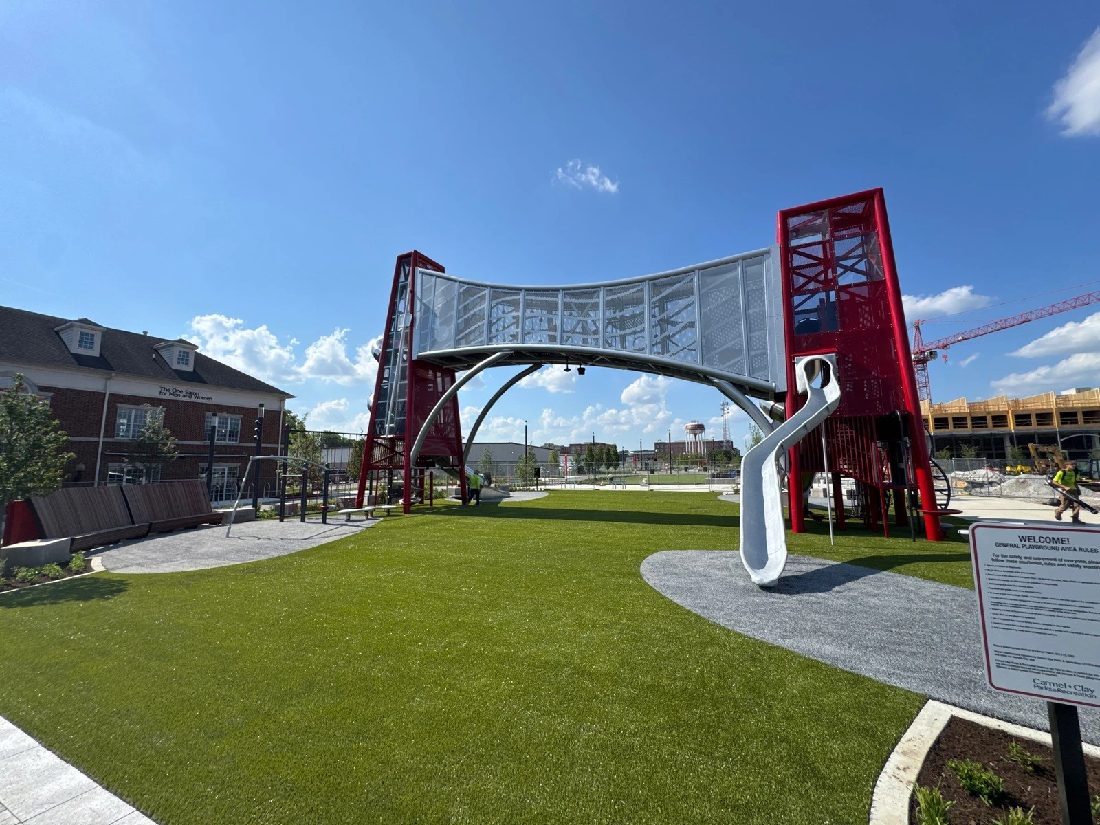 Modern playground with red steel arch structure, slide, and lush artificial turf at Carmel's Monon development, Indiana.