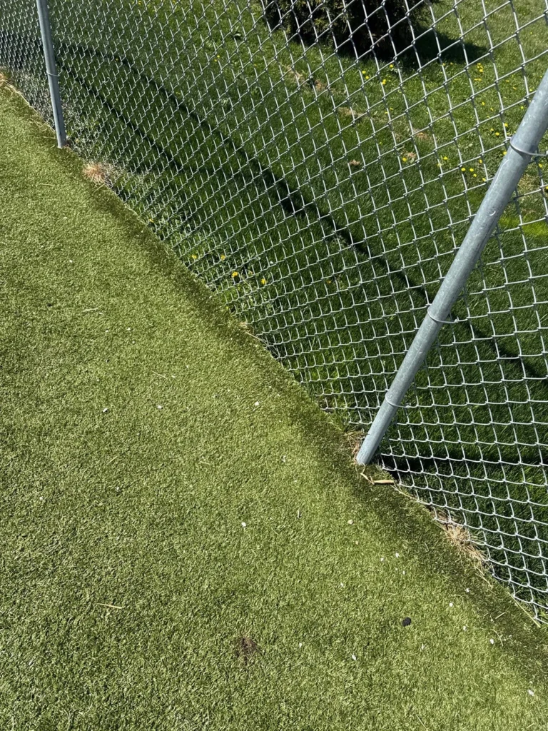 K9Grass artificial turf edge repair along chain-link fence post at Johnson County Animal Shelter pet yard.