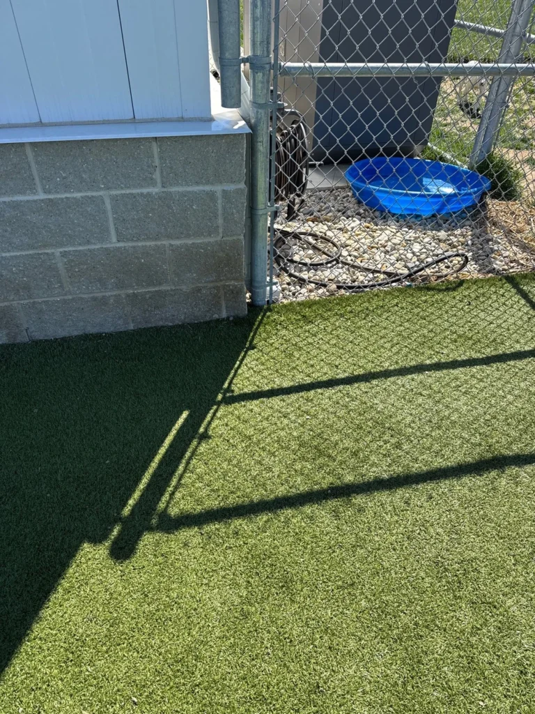 K9Grass artificial turf installed along chain-link fence at Johnson County Animal Shelter pet yard with gravel border and blue water bowl.