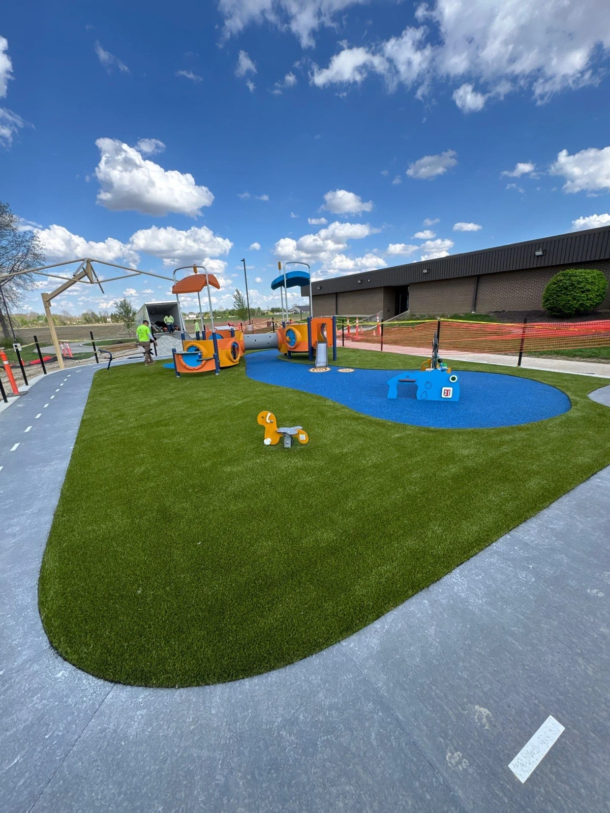 Newly installed synthetic playground turf with blue rubber safety surfacing surrounds colorful play structures at Mt. Vernon Park, Fortville, IN.