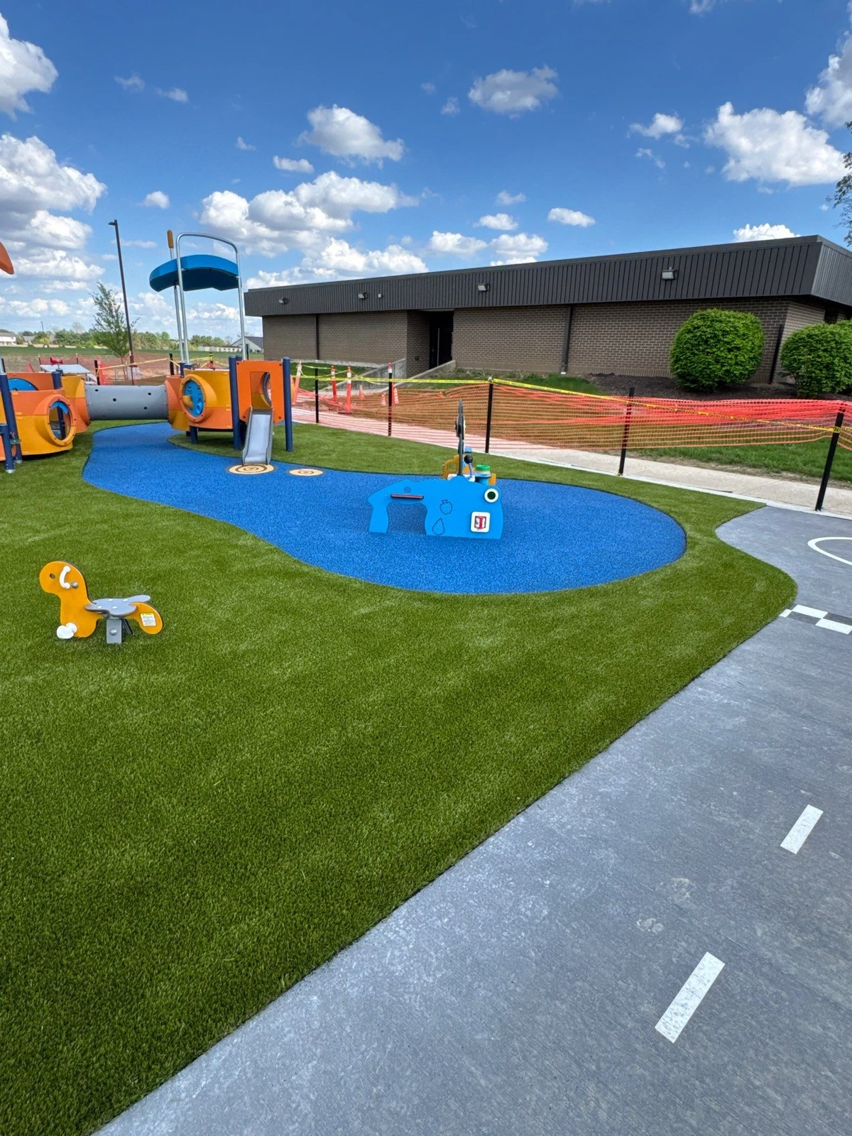 Colorful municipal playground with blue rubber safety surface and synthetic turf installation, Fortville IN park facility.