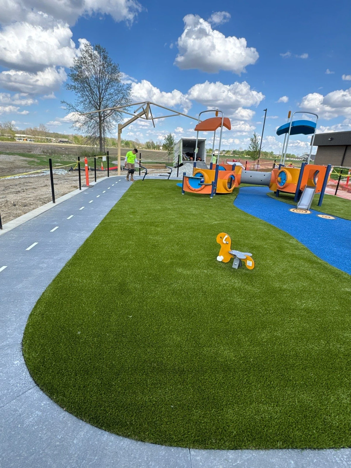 ForeverLawn Playground Grass installation at Mt. Vernon Park Fortville IN with colorful play structures, blue rubber surfacing, and paved path.