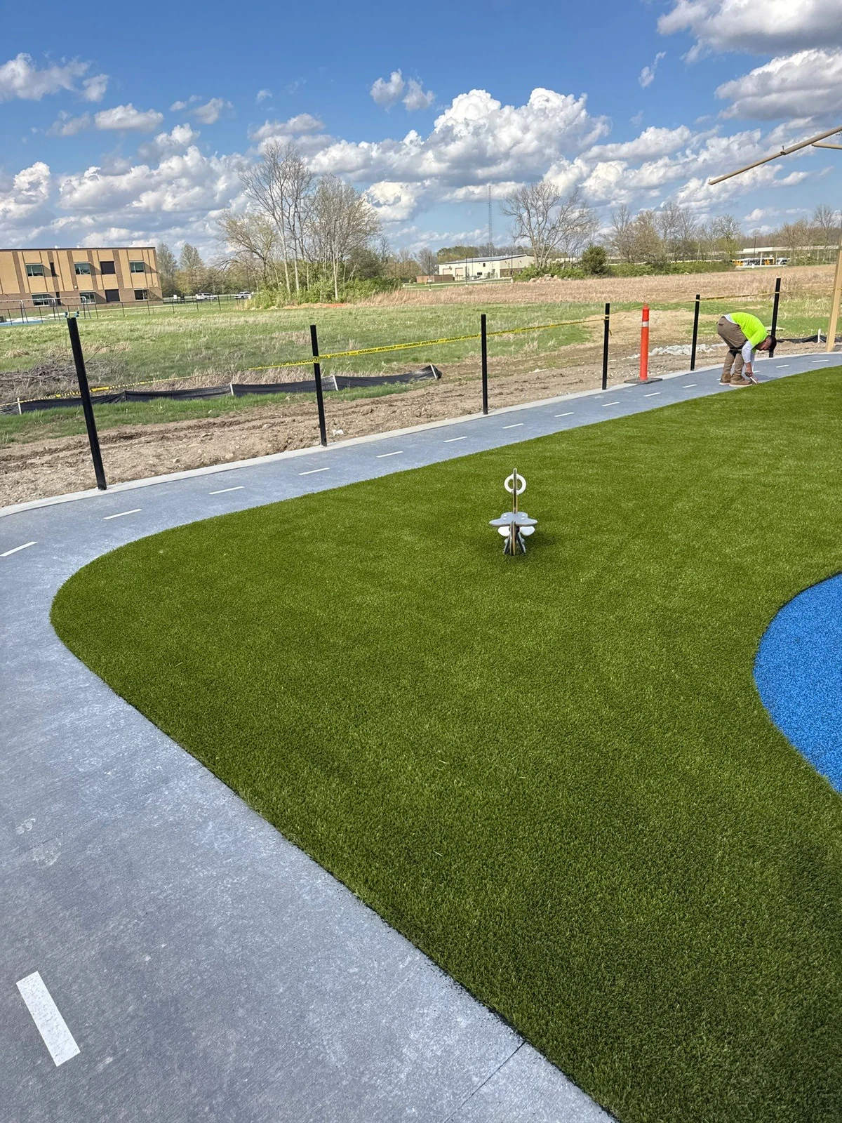 Freshly installed Playground Grass artificial turf surrounds a curved concrete path at Mt. Vernon municipal park in Fortville, IN, with worker finishing installation.