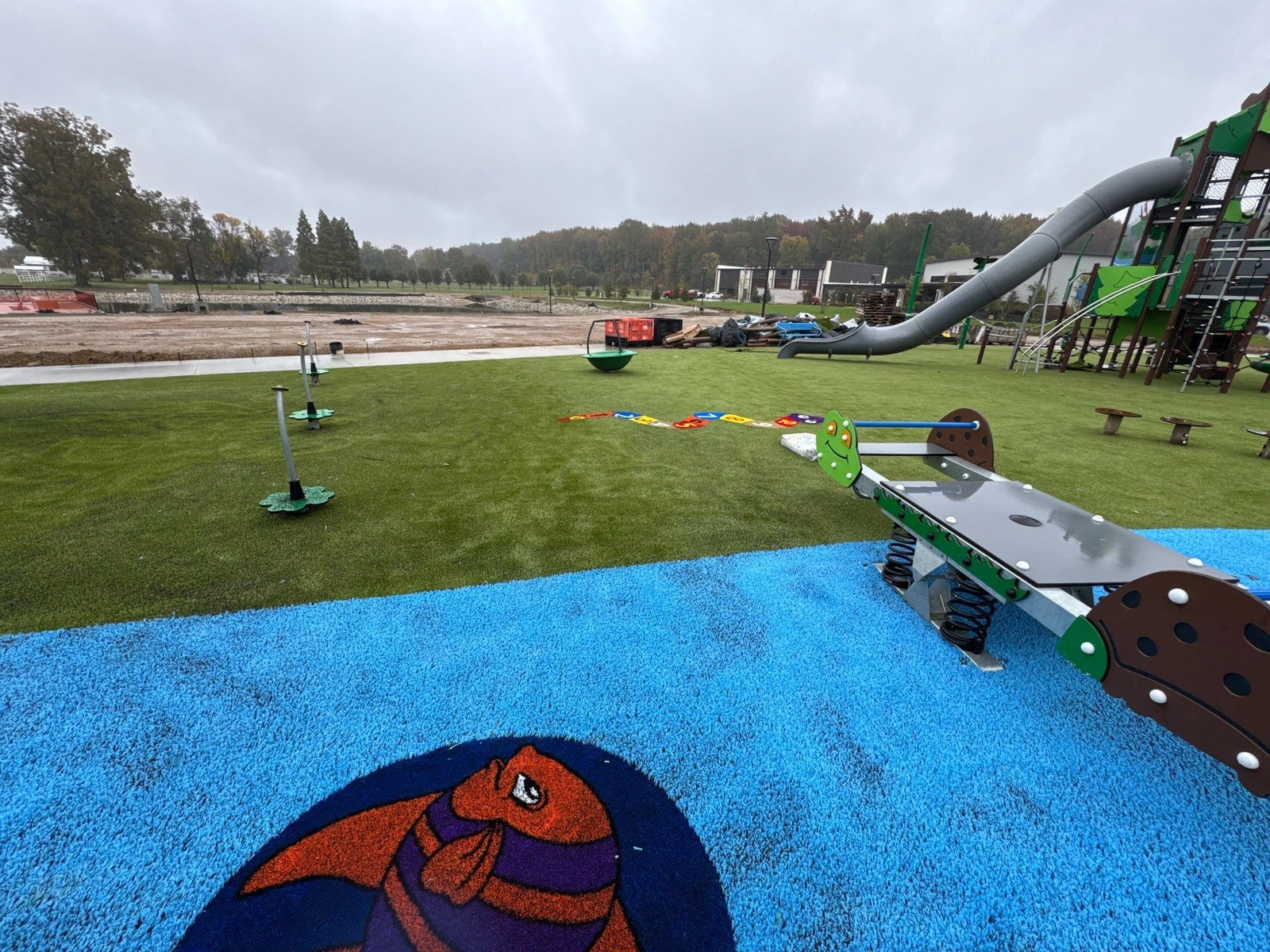 ForeverLawn Playground Grass installation in blue and green at Ohio Township park with tube slide, spring riders, and construction area beyond.