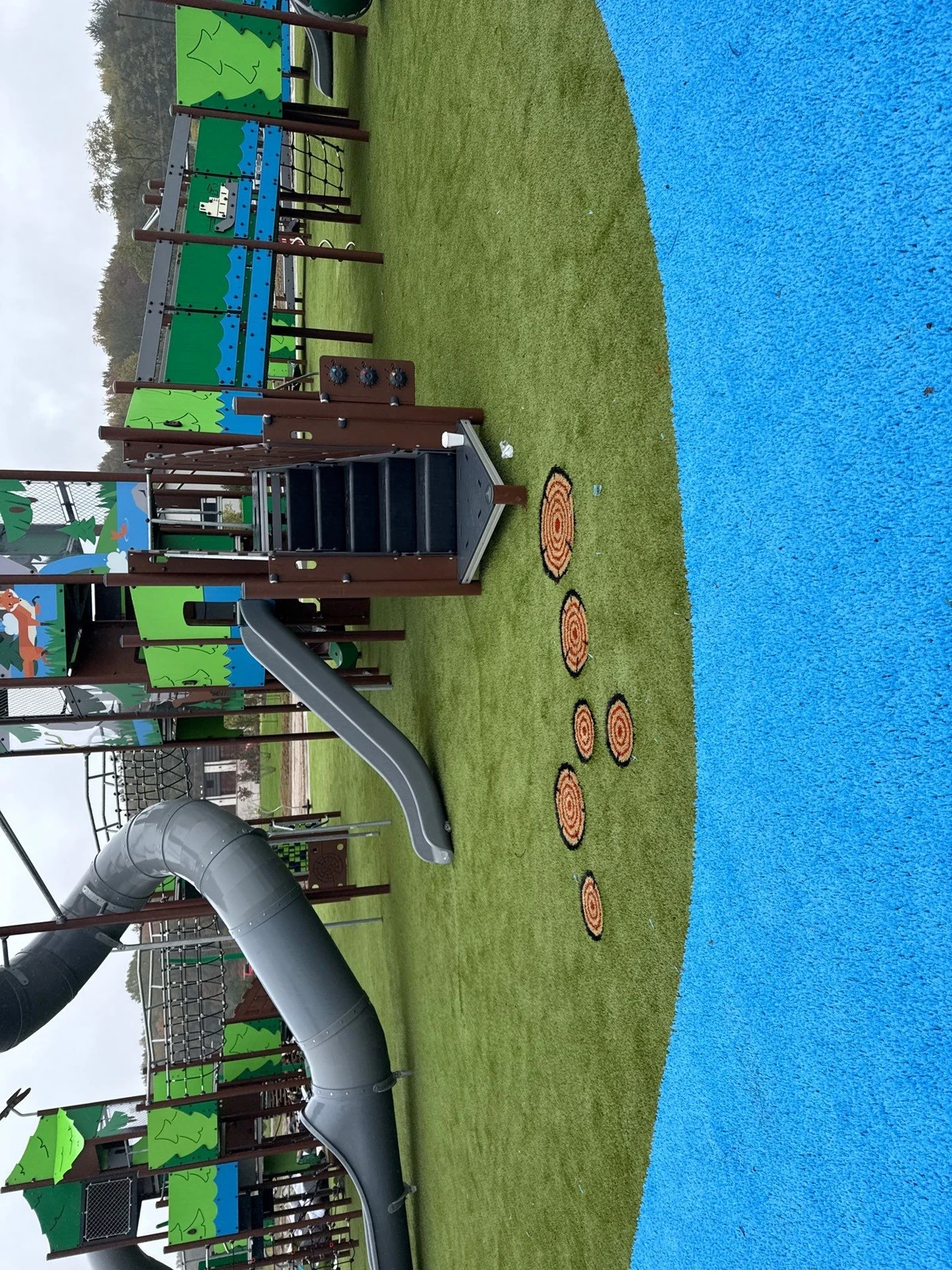 ForeverLawn Playground Grass installation at Ohio Township park with blue safety surfacing beside green turf and colorful play structure with slides.