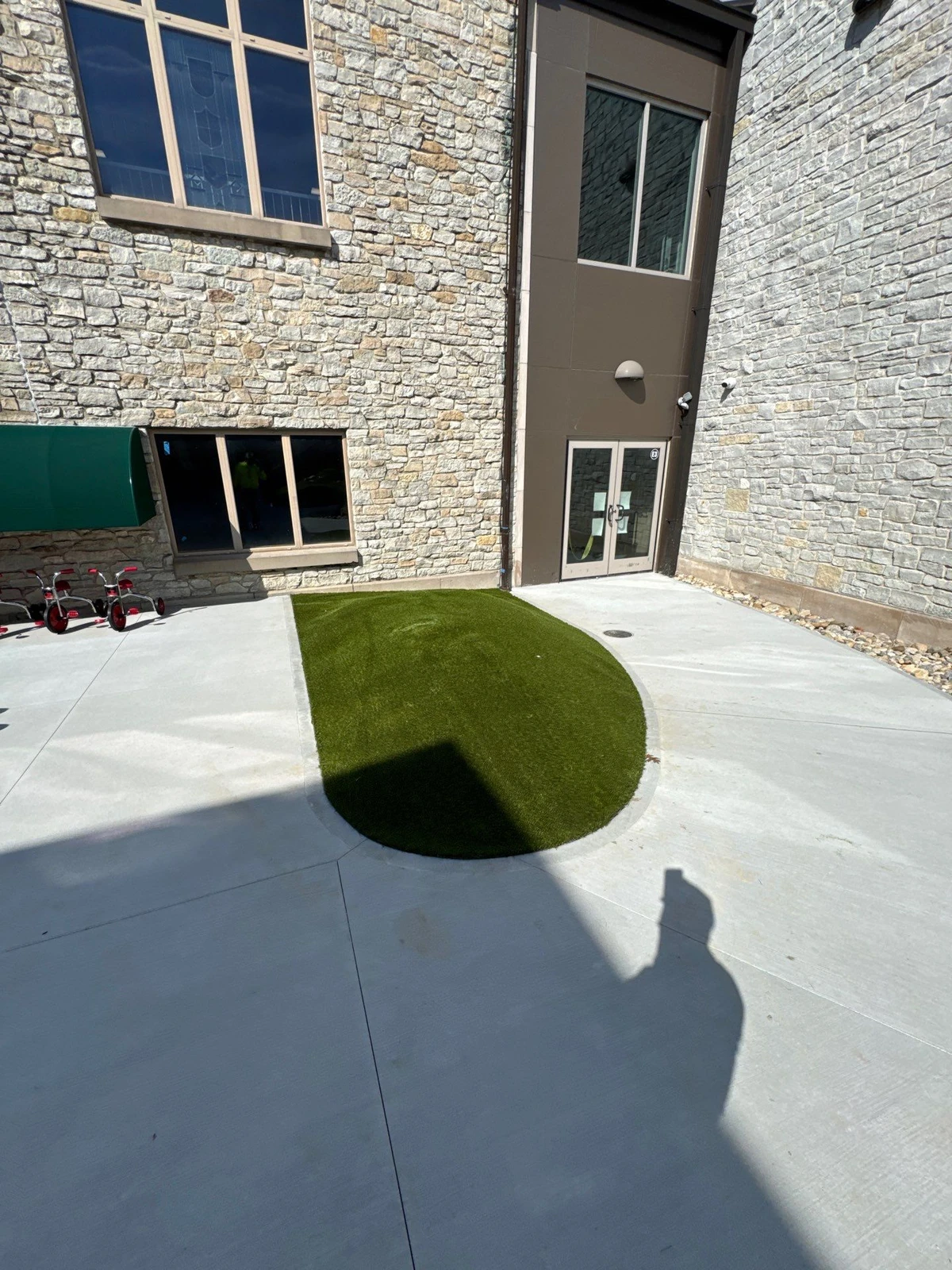 Artificial playground grass installed in curved concrete cutout at Indianapolis school courtyard with stone building exterior.