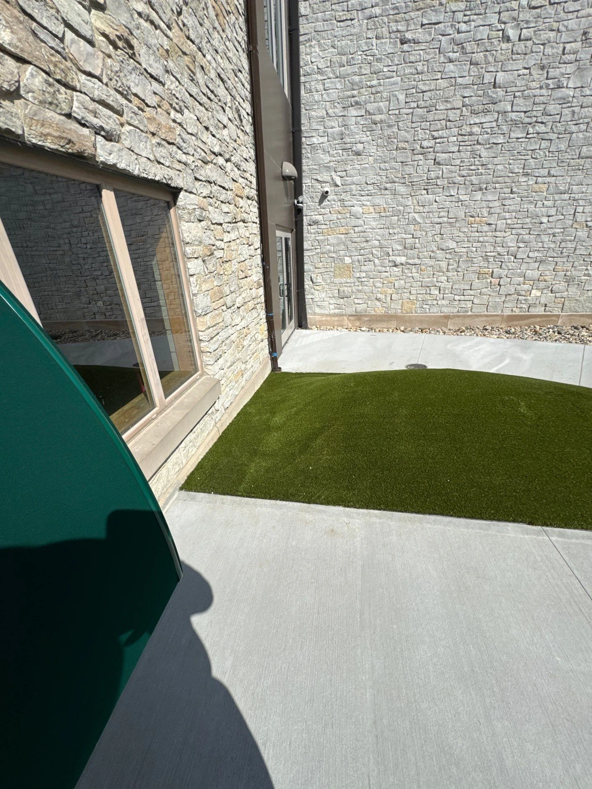 Artificial playground grass strip installed in courtyard between stone building walls with concrete pavers, Indianapolis school.