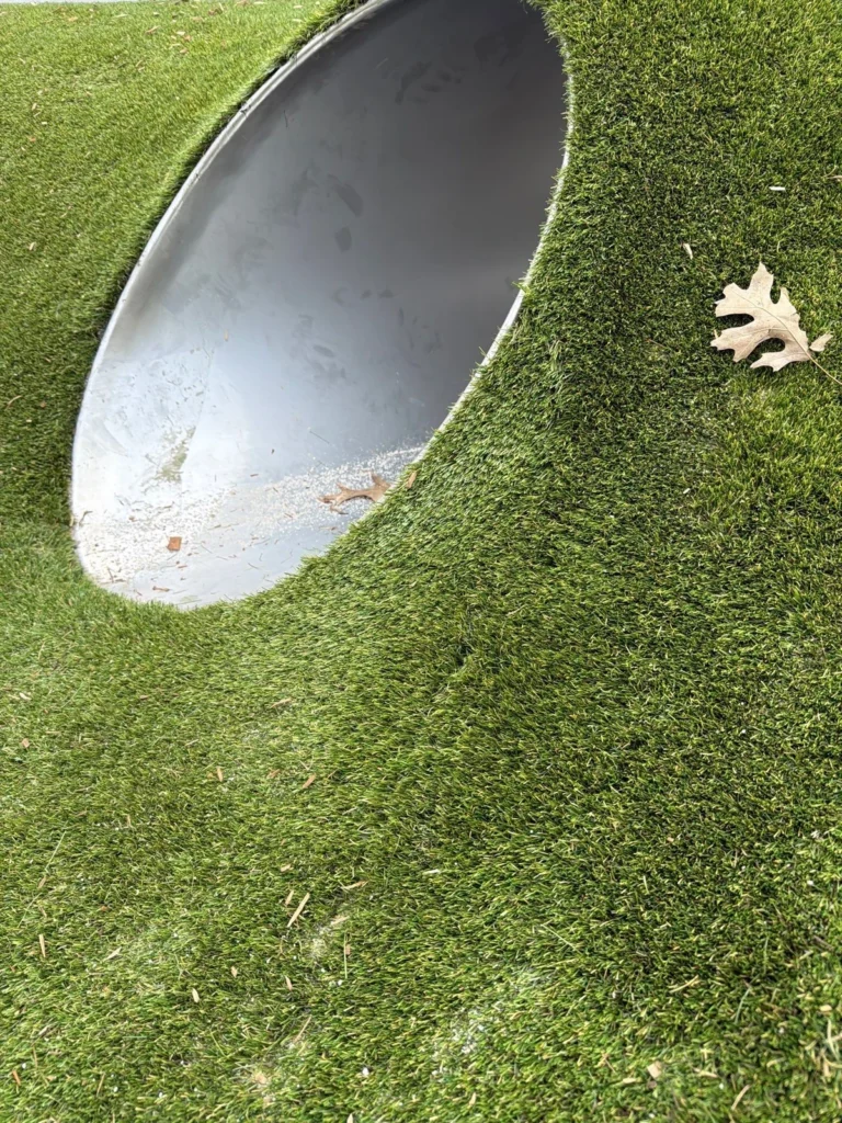 Artificial playground grass wrapped around a curved metal tunnel opening at St. Richards school Indianapolis.